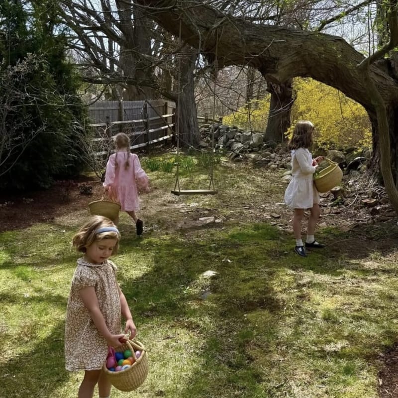 three girls carrying Easter baskets during an outdoor egg hunt in a backyard garden with a rope swing and stone wall