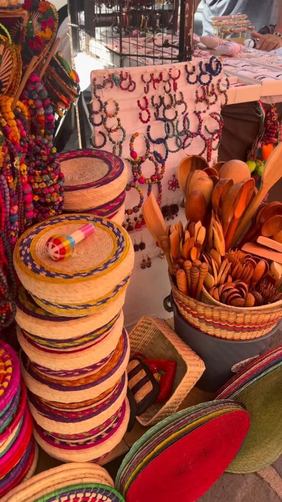 Colorful artisan market stall in Mexico City with stacked woven baskets, wooden spoons in a wicker holder, and beaded jewelry on display