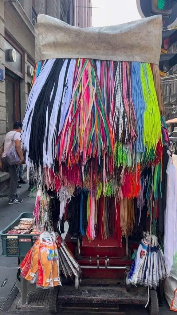 Street vendor cart draped with hundreds of colorful shoelaces in Mexico City