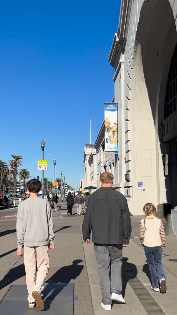 Two kids and an adult walking along the Embarcadero in San Francisco on a sunny day, Ferry Building facade on the right