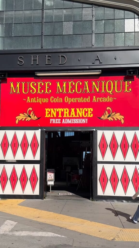 Musee Mecanique entrance at Shed A on the San Francisco waterfront, with a red banner reading "Antique Coin Operated Arcade, Entrance, Free Admission"