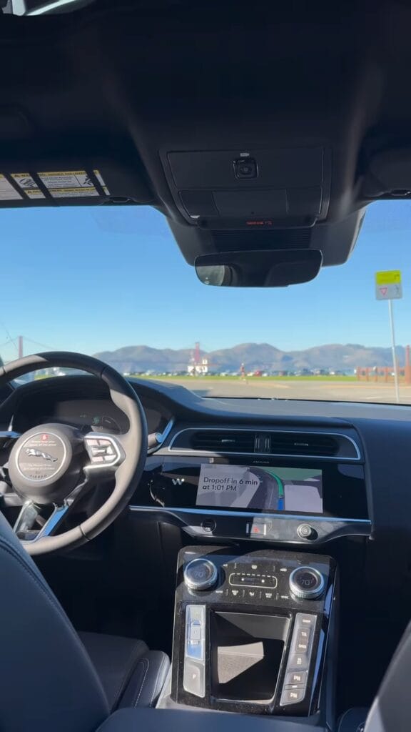 Interior view of a Waymo Jaguar I-PACE robotaxi dashboard with navigation screen showing a drop-off in 6 minutes, Golden Gate Bridge visible through the windshield