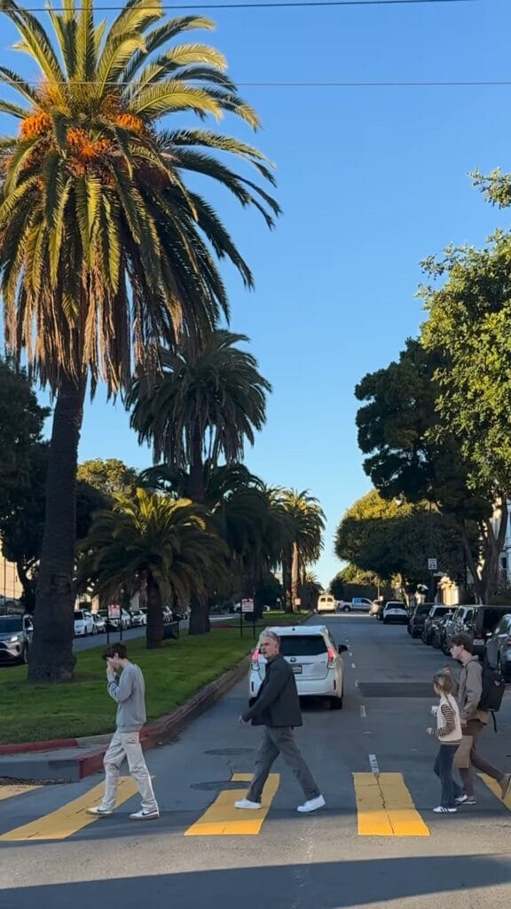 Four people crossing a yellow-painted crosswalk on a palm-lined San Francisco street under a clear blue sky