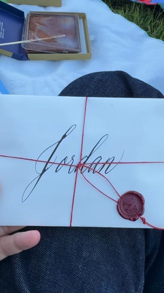 White envelope addressed to Jordan in calligraphy, tied with red twine and sealed with a red wax seal, held at an outdoor picnic