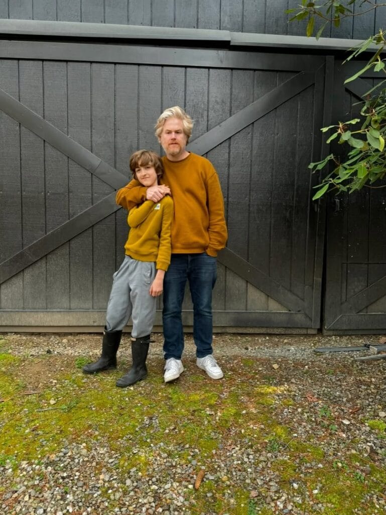 Paul Ferney and a child wearing matching mustard sweatshirts, standing together in front of a dark barn door